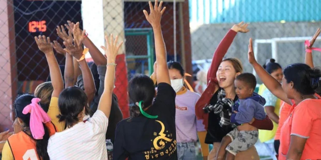 A group of people joyfully raising their hands indoors, one holding a child.
