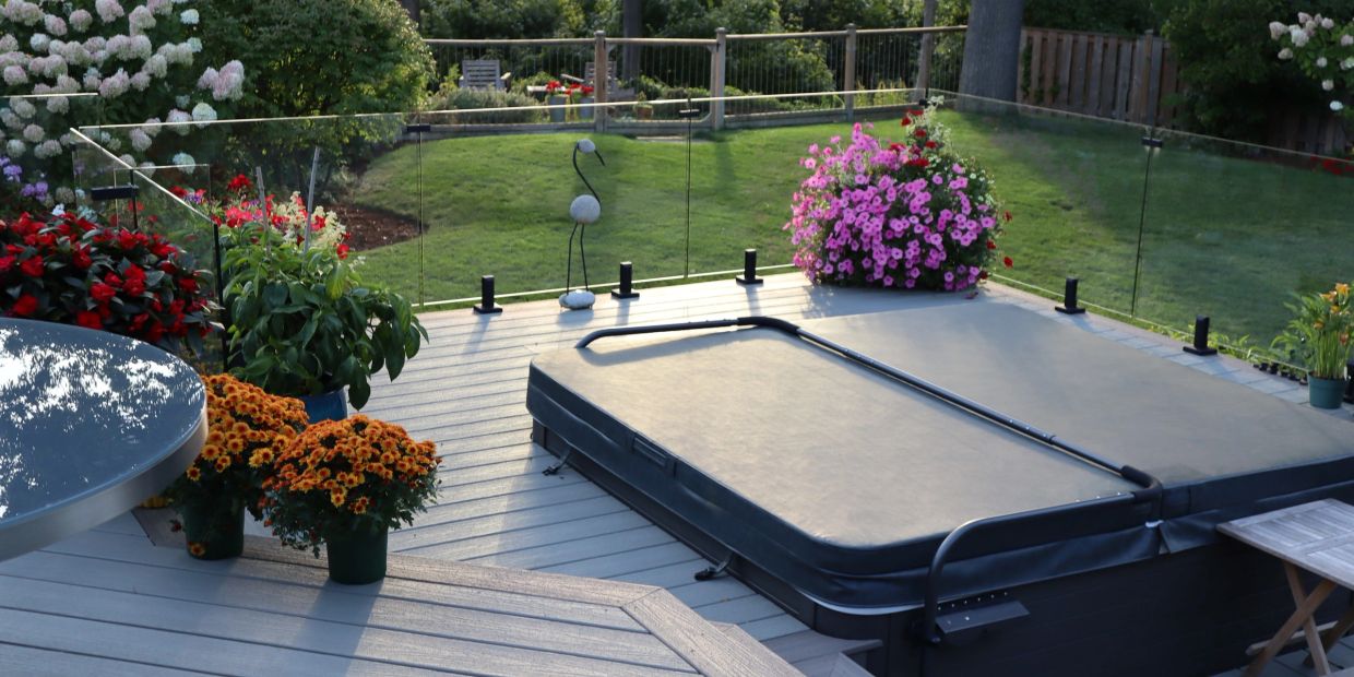 a trex composite deck with integrated hot tub and frameless glass railing looking out into a garden