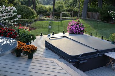 Grey composite deck with hot tub built in and frameless glass railing looking out onto a lush yard