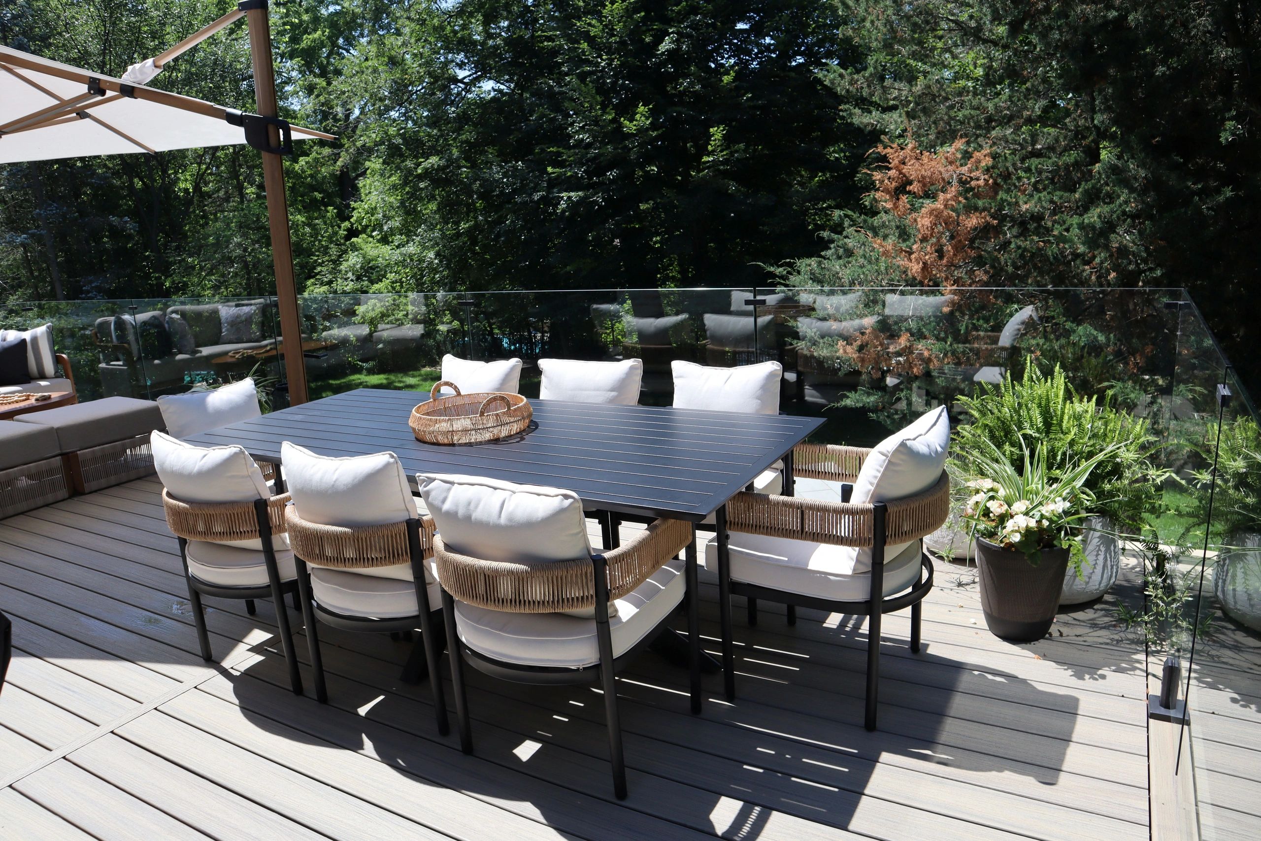 black dining table with chairs and white cushions on a Trex composite deck with glass railing 