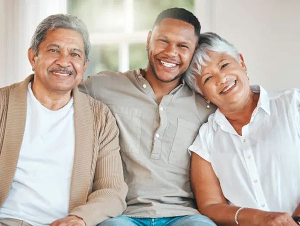 Three generations smiling together on a couch at home.