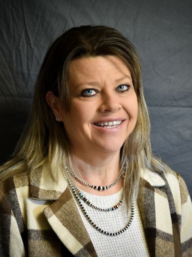 Smiling woman in checkered jacket and layered necklaces.