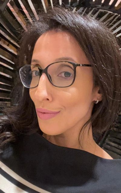 Woman with glasses smiling in a dimly lit space.