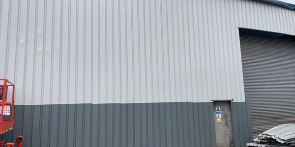 Industrial building exterior with a large gray and white wall and a metal rolling door.