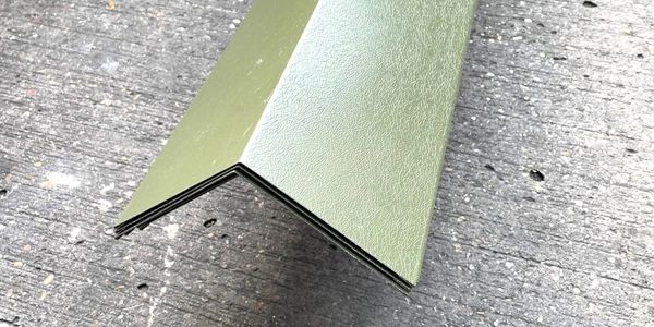 Stack of green metal corner guards on a rough surface.