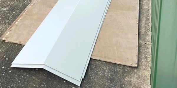 White metal roofing panels stacked on a concrete surface with wooden boards underneath.