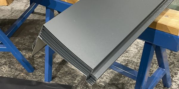 Stacked gray metal panels resting on blue sawhorses in a workshop.