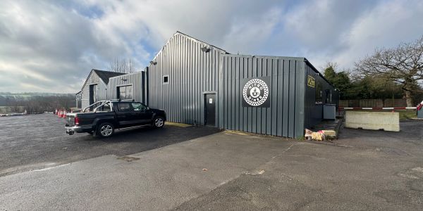 Gray industrial building with a black pickup truck parked outside under a cloudy sky.