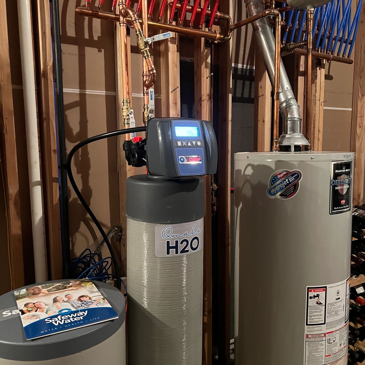 Water softener system and water heater installed in a basement with exposed pipes.