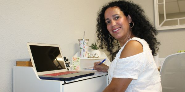 Woman working at a desk with a laptop, smiling at the camera.
