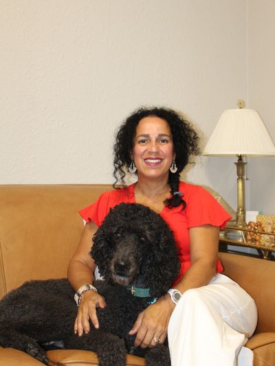 A photo of a woman and a black poodle sitting on a couch.