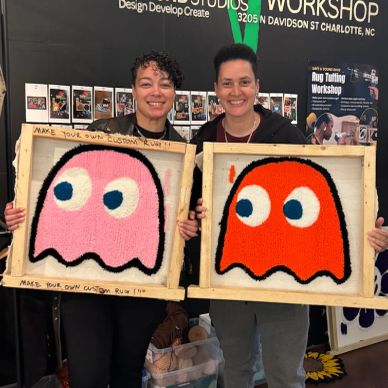 Two people holding handmade ghost-themed rug art.
