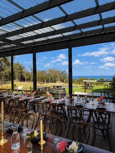 Elegant outdoor dining setup with wood tables overlooking a scenic landscape and ocean.