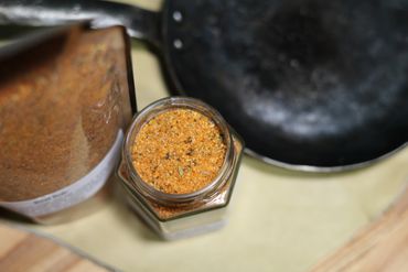 Jar of spices on butcher block table next to cast iron pan on leather swatch.