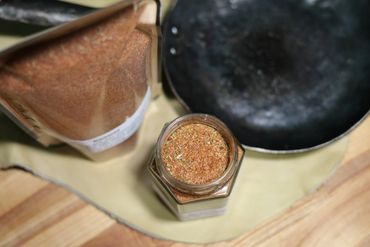 Jar of spices on butcher block table next to cast iron pan on leather swatch.