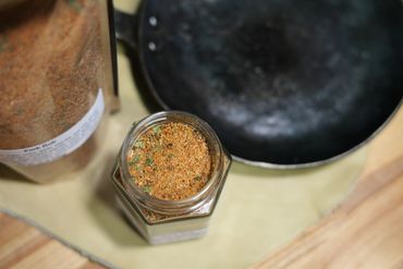 Jar of spices on butcher block table next to cast iron pan on leather swatch.