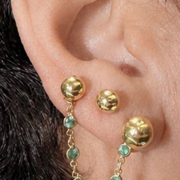 Close-up of ear with gold earrings connected by a chain with green stones.