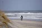 Surfer walking on sandy beach towards ocean waves.