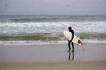 Surfer in a wetsuit holding a surfboard, gazing at the ocean waves.