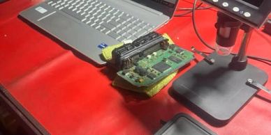 Laptop, circuit board, and microscope on a red table.