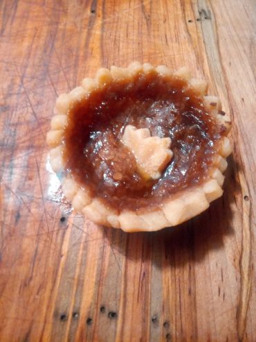 A small tart with a decorative pastry heart on top, placed on a wooden surface.