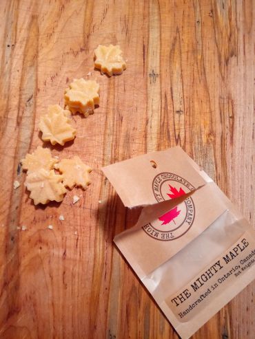 Maple leaf-shaped candies spilling from a branded package on a wooden surface.