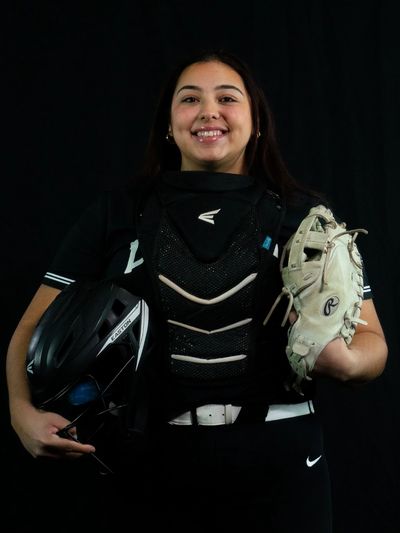Softball player with helmet and glove smiling at camera.