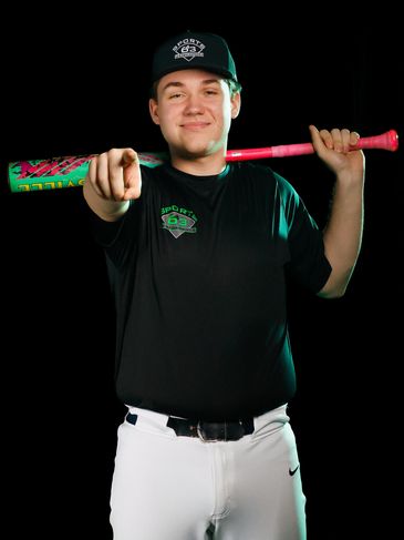 Young baseball player posing with bat and pointing forward.