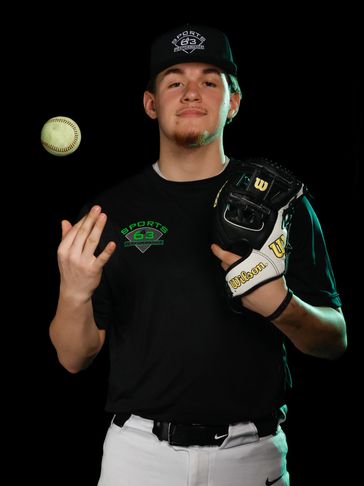 Young baseball player posing with a glove and ball against black background.