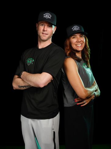 Two people wearing matching caps and casual sportswear, standing back-to-back.