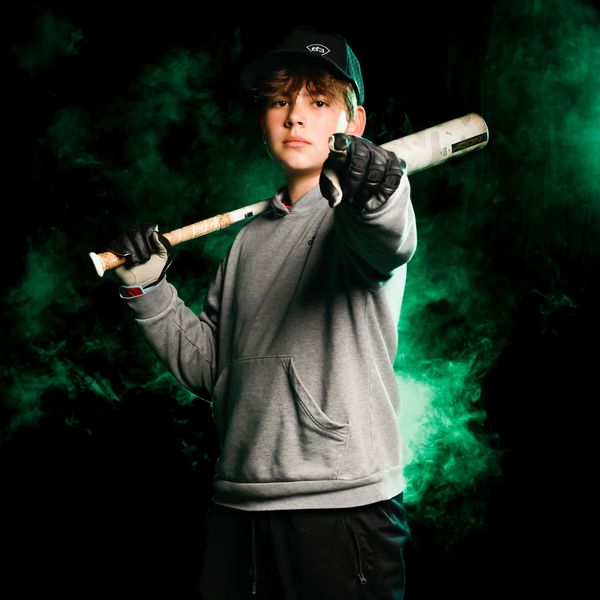 Teen baseball player holding bat confidently against green smoke.