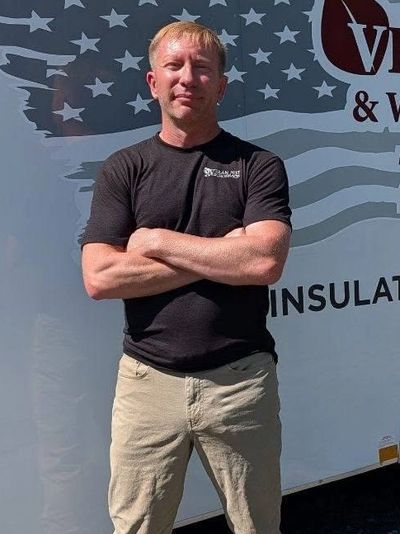Owner Morgan Jones stands by a white truck, wearing black unifrom tshirt and khaki workpants, arms f