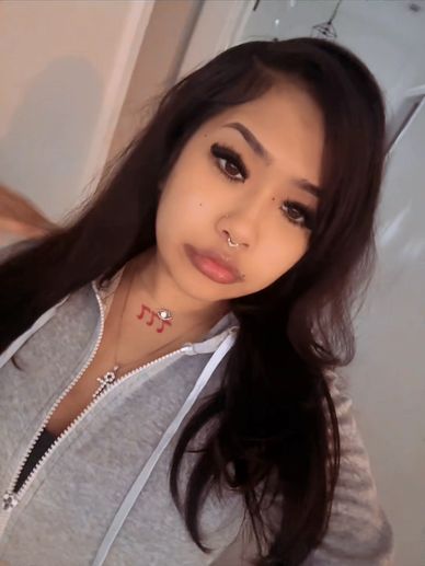 Young woman with long dark hair and septum piercing in a gray hoodie.