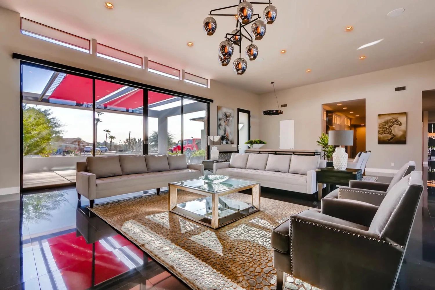 Modern living room with neutral sofas, stylish armchairs, and large glass doors opening to a patio.