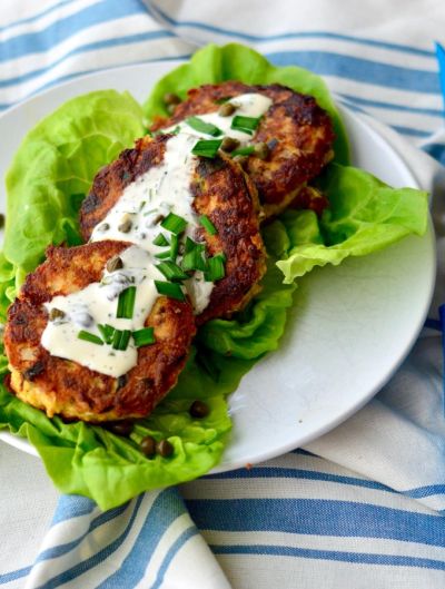 Three crispy crab cakes with creamy sauce and chopped chives on lettuce.