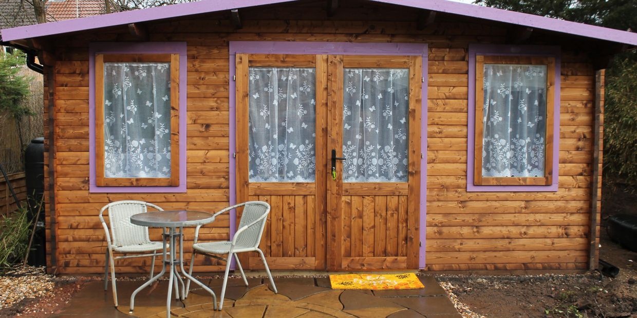 Wooden garden shed with purple trim and outdoor seating on a decorative patio.