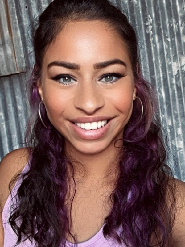 Smiling woman with purple hair and hoop earrings.