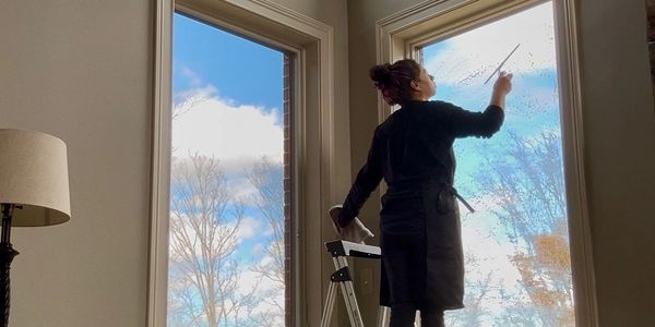 Person cleaning tall windows using a ladder.