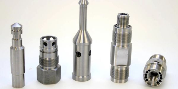 Five precision-machined metal components with varied shapes and threading.