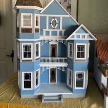 Blue dollhouse with white trim and multiple windows.