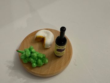 Miniature food items including grapes, cheese, and a bottle on a wooden plate.