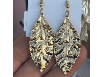 Gold-colored leaf-shaped earrings held in a hand.