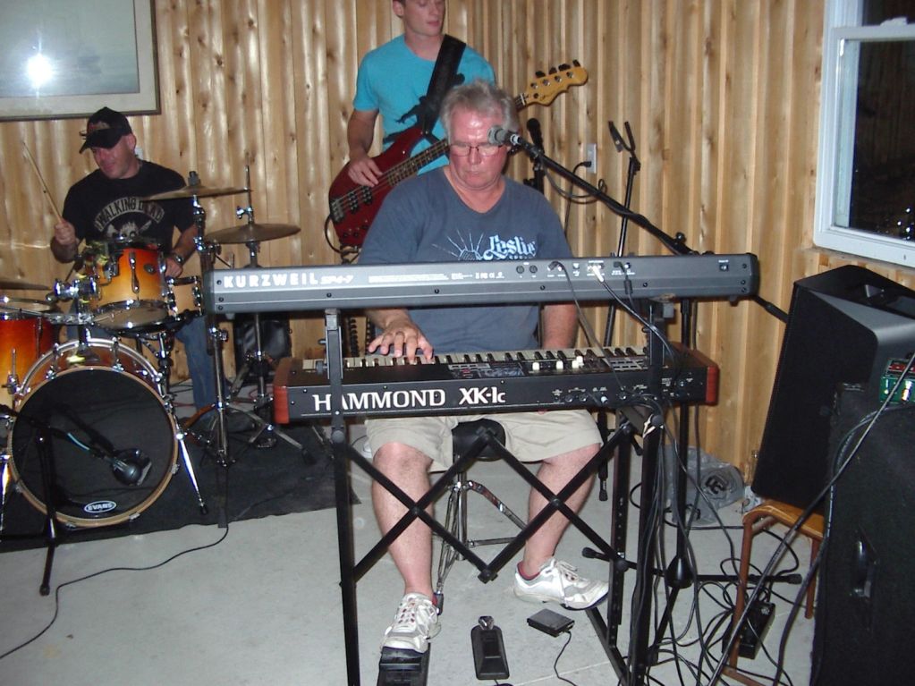 A band performing indoors with keyboard, bass, and drums.
