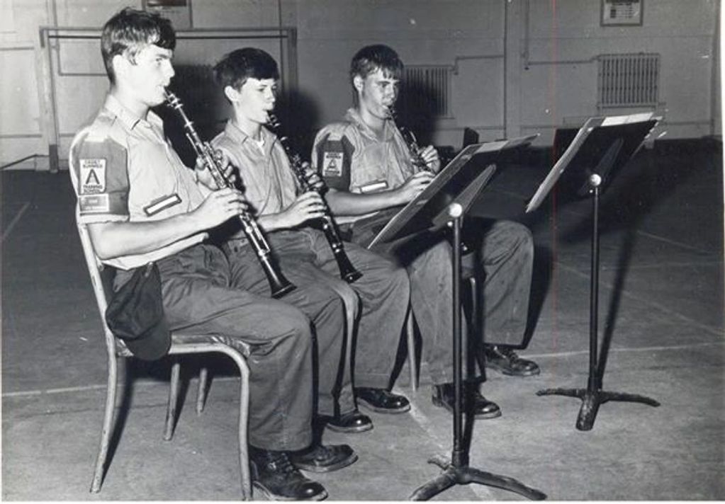 Three young musicians in uniform playing clarinets indoors.