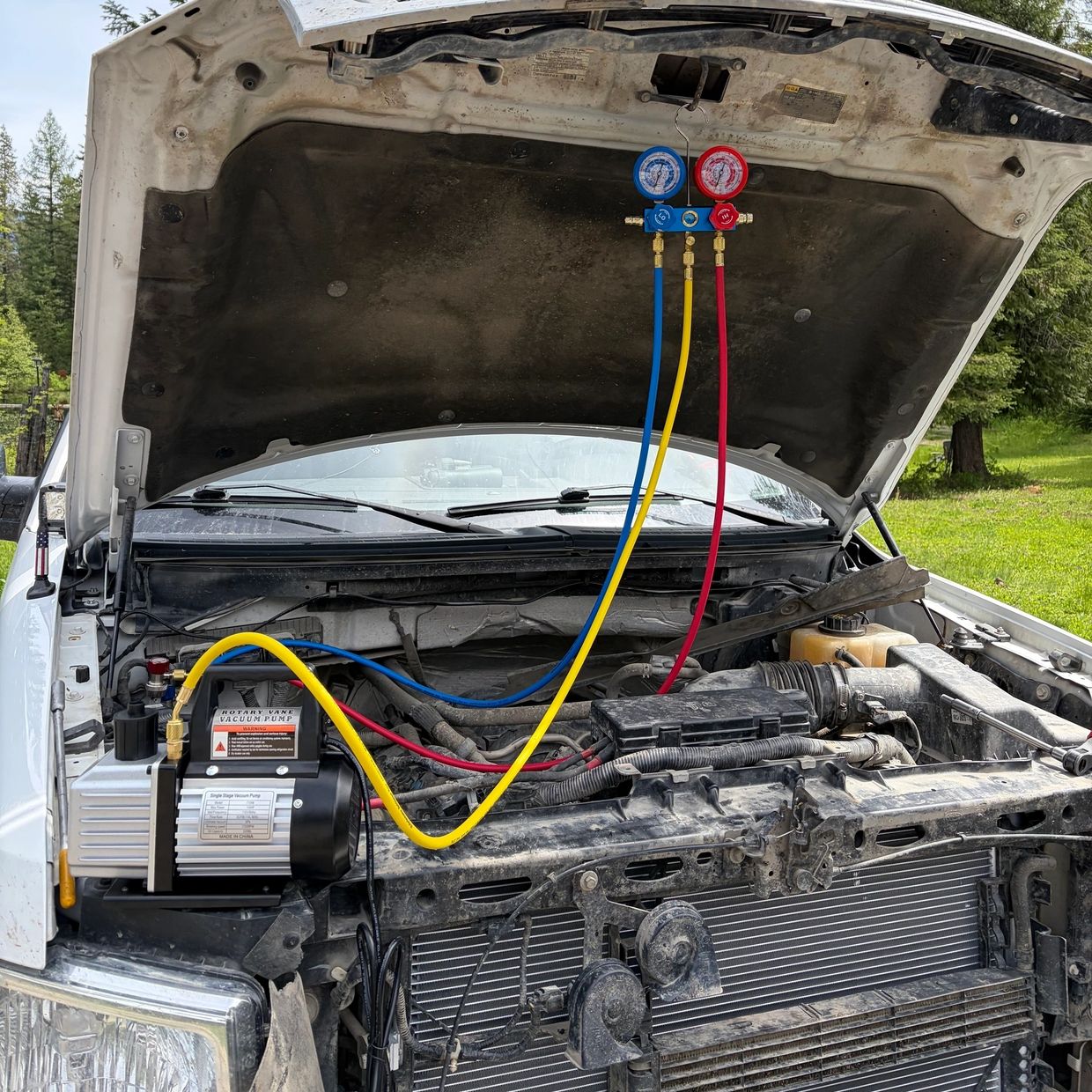 Car air conditioning system being serviced with vacuum pump and gauges.