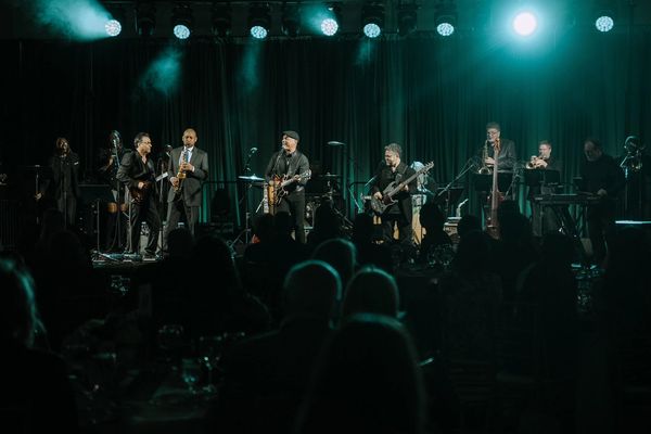 A band performing live on stage with various instruments under bright lights.