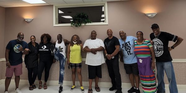 A diverse group of people smiling and posing indoors against a wall.