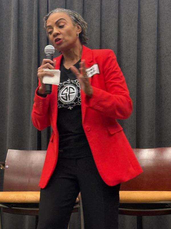 Woman in red blazer speaking into a microphone.