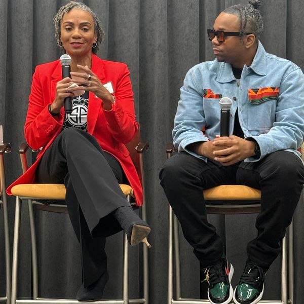 Two individuals holding microphones, seated, engaged in conversation at an event.