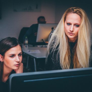 Two women joined together in front of a computer, trying to solve a problem together.